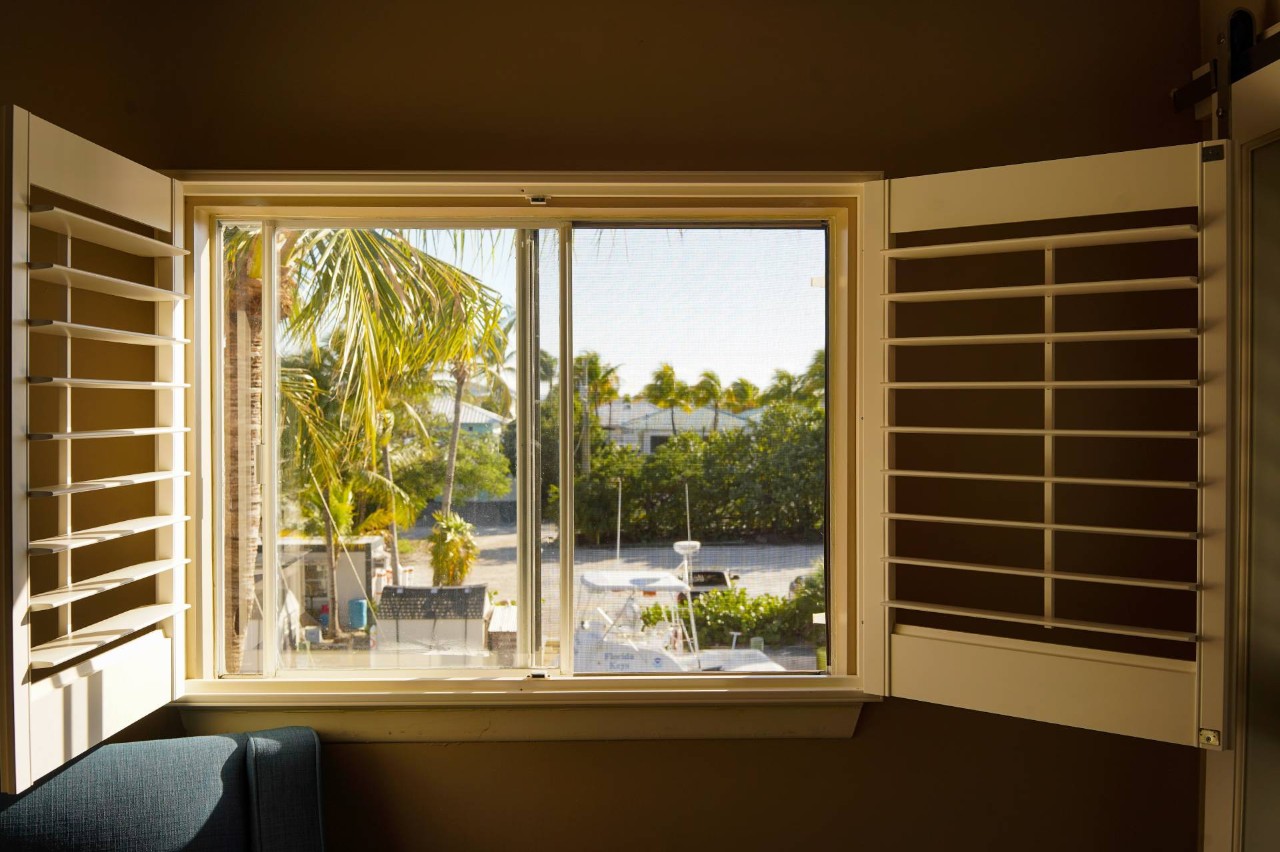 Open white window shutters overlooking a stunning Florida view with a patio and palm trees at Custom Window Decor of Jupiter near Jupiter, FL
