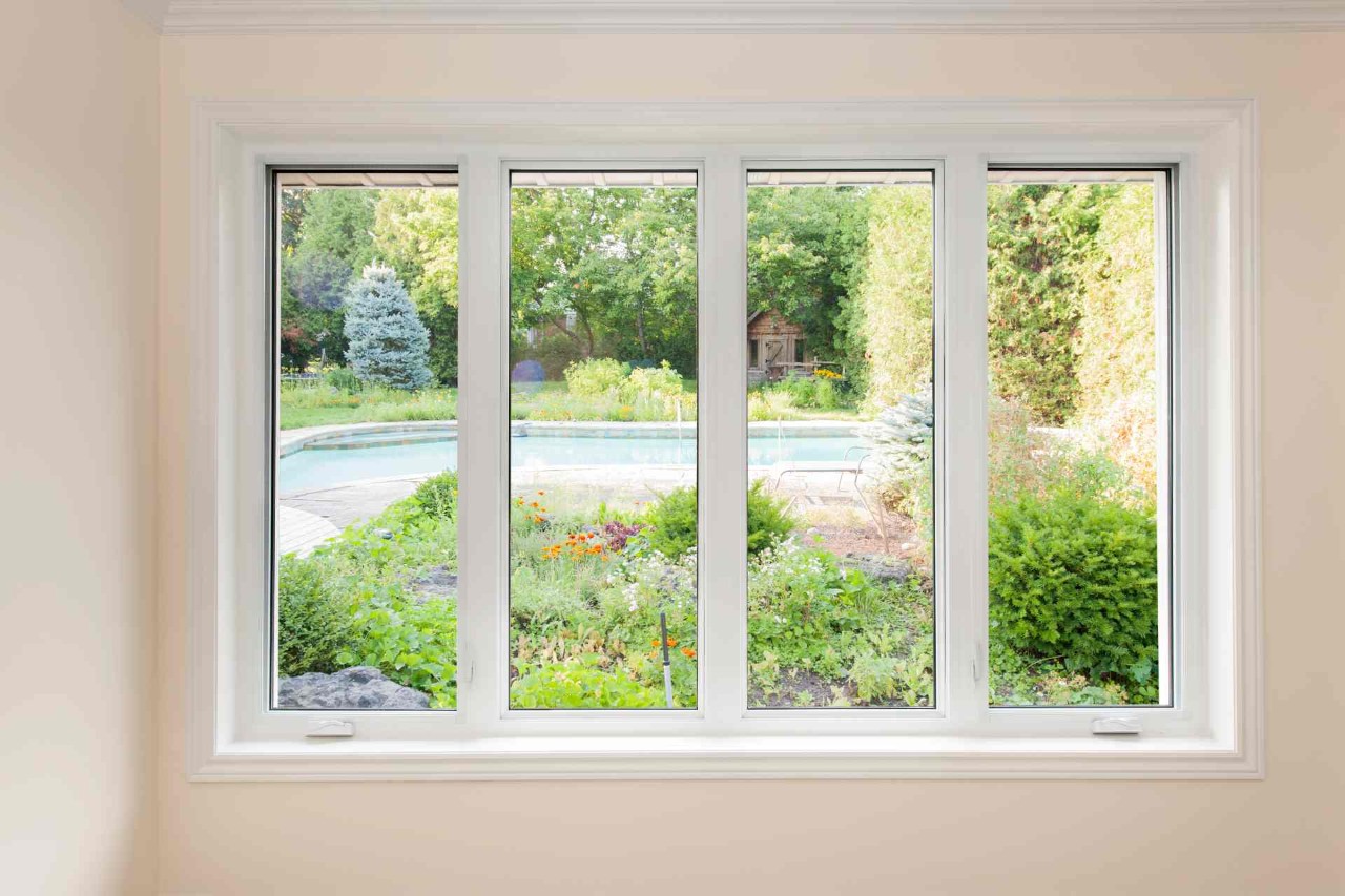 A casement window overlooking a beautiful backyard with greenery and flowers surrounding an in-ground pool at Custom Window Decor of Jupiter near Jupiter, FL